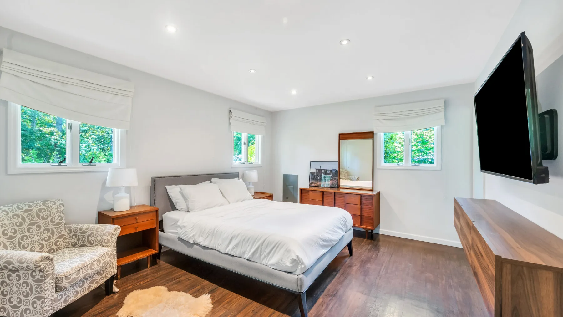 A bright bedroom with a bed, patterned seating, and a wall-mounted television.