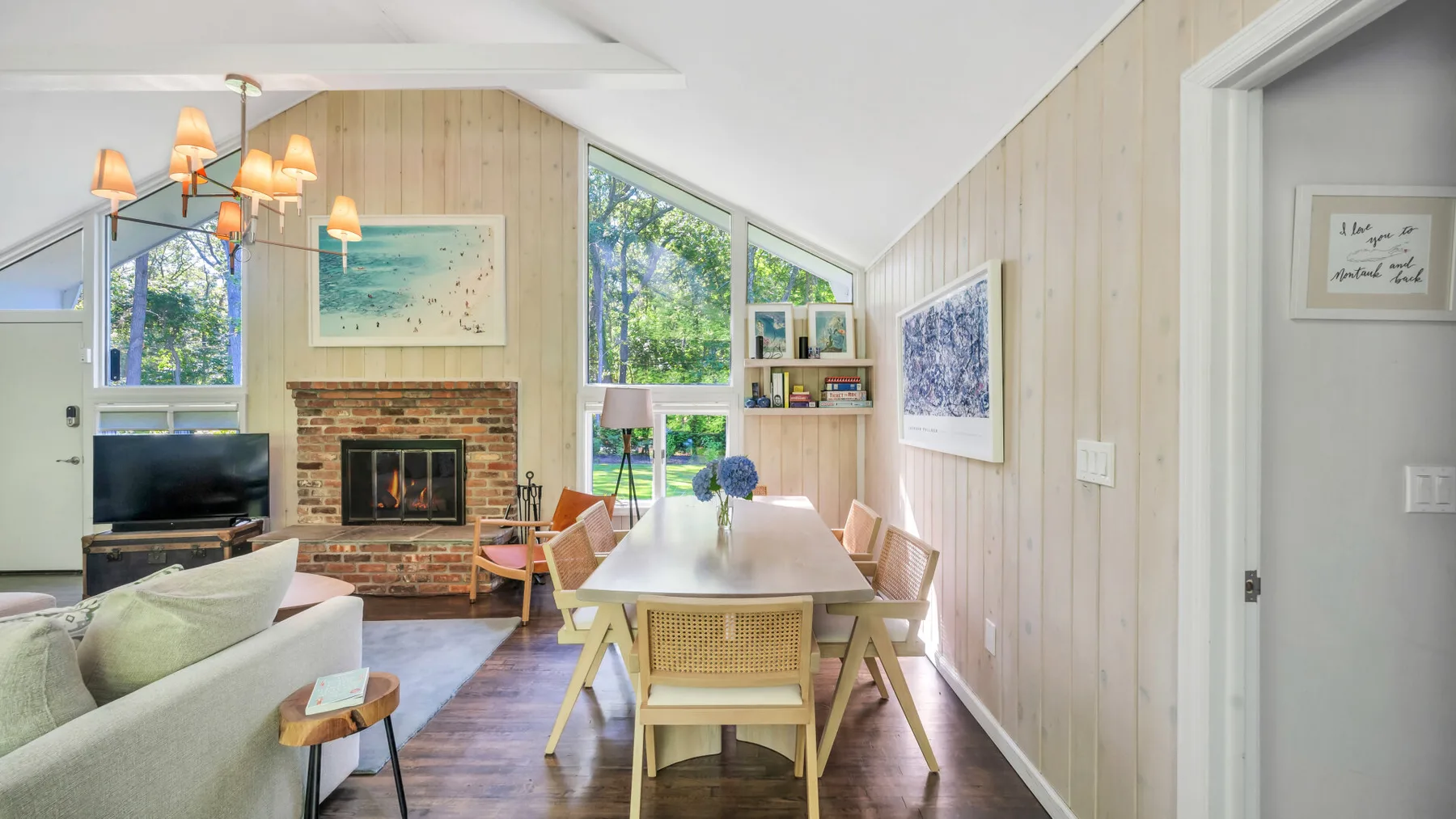 A bright living and dining area has a fireplace, large windows, and a dining table.