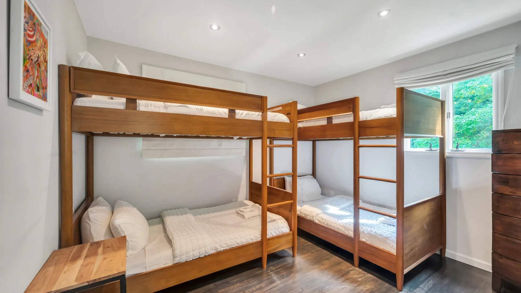 A bedroom with wooden bunk beds and a window overlooking greenery.