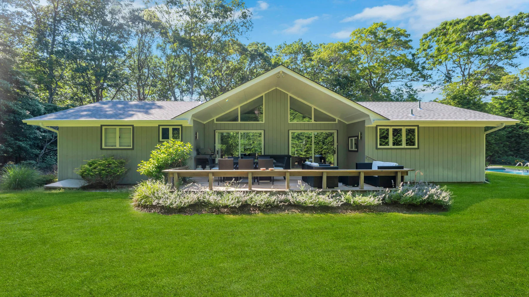 A house with a broad lawn and a raised outdoor seating area.