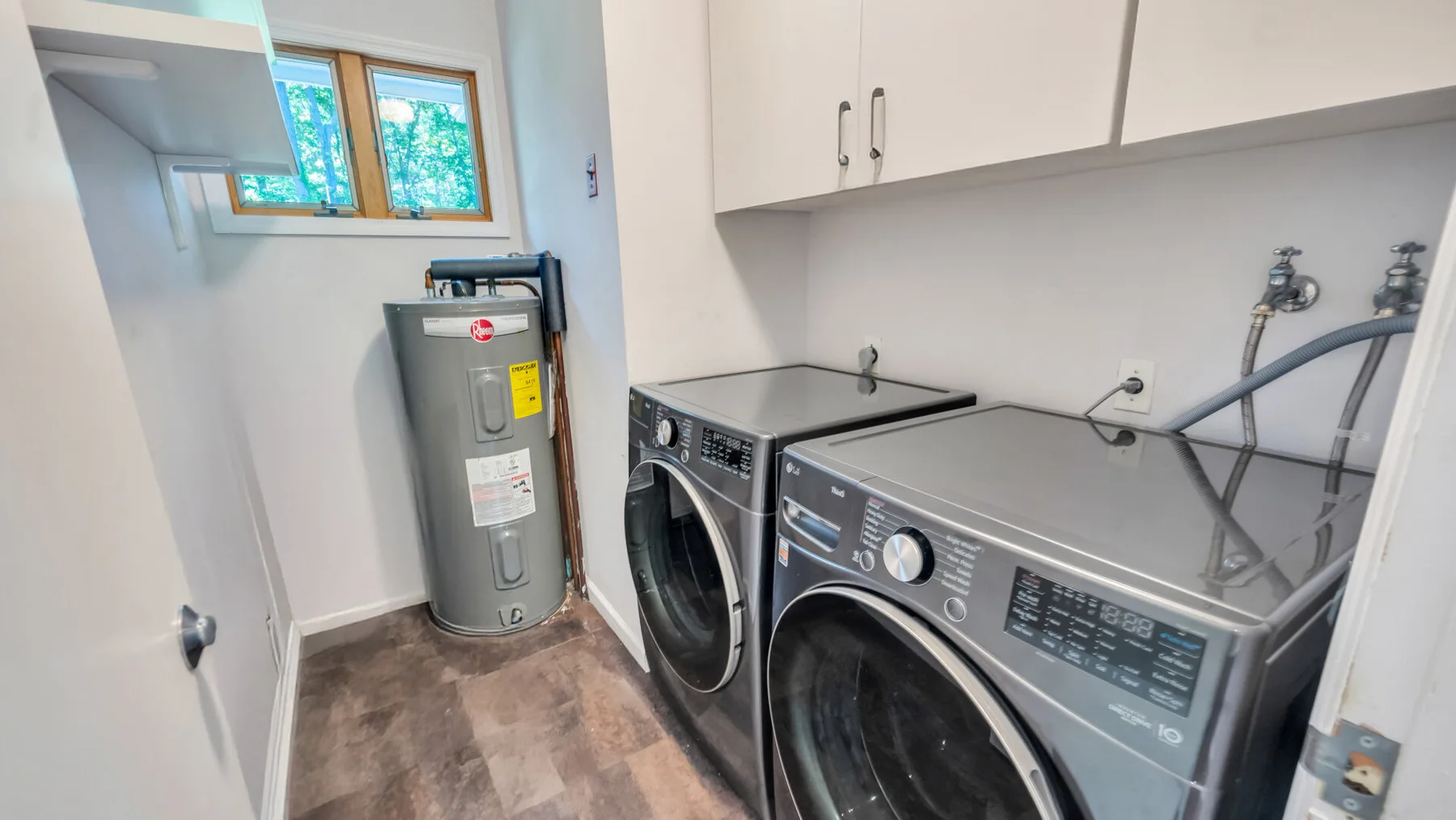 A laundry room with a washer and dryer beneath white cabinets.