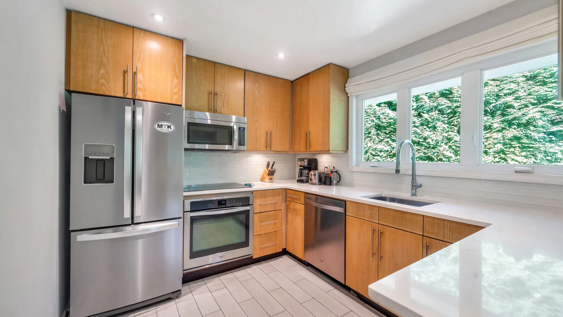 A bright kitchen with wooden cabinets, stainless steel appliances, and a window above the sink.