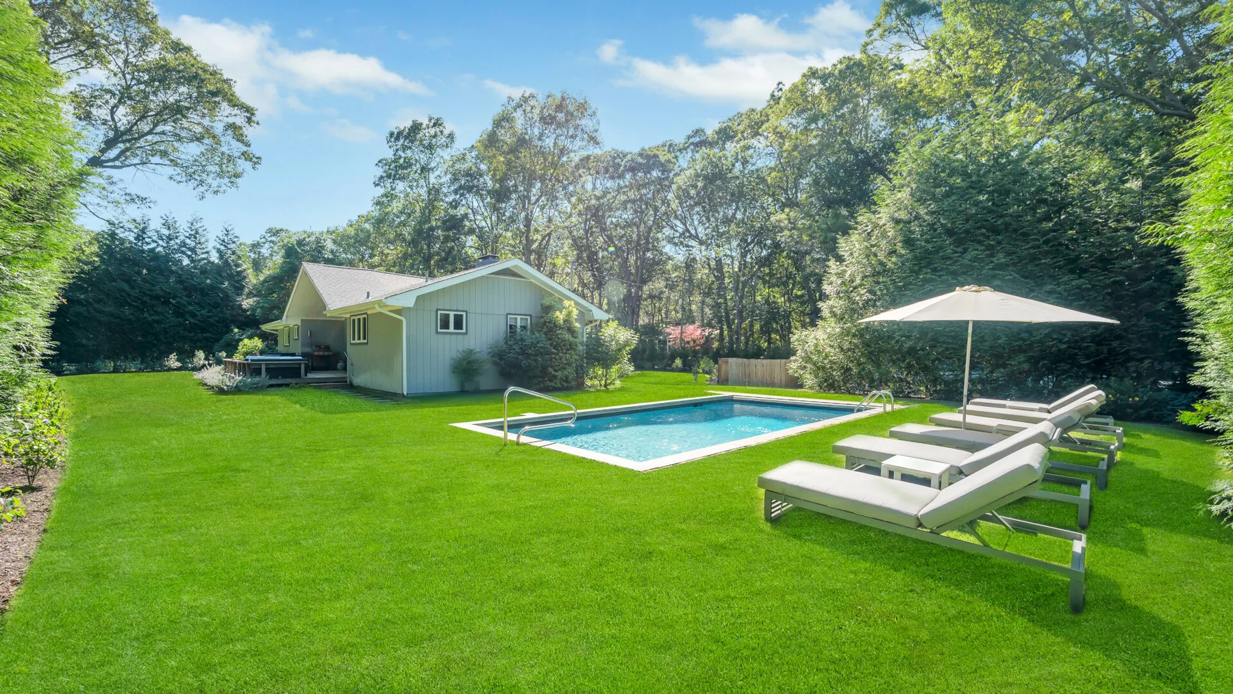 A backyard swimming pool sits beside a small house and outdoor loungers.