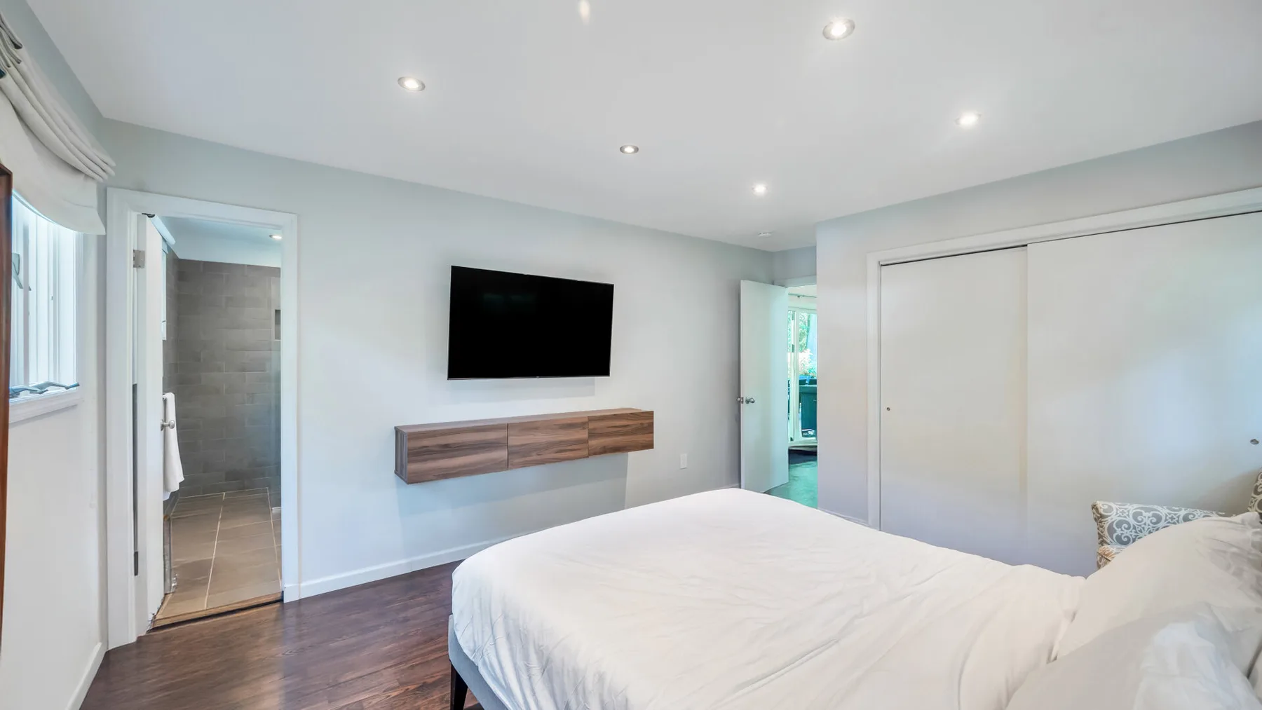 A bedroom with a bed, wall-mounted television, and a doorway to a bathroom.