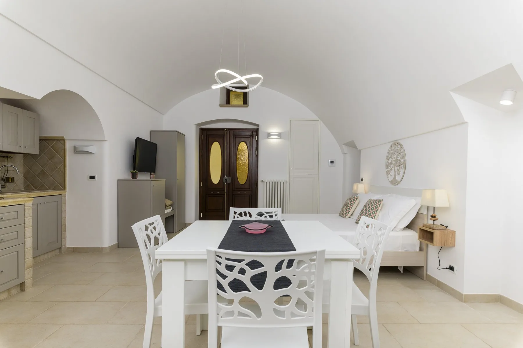 A bright open-plan room with a dining table, kitchenette, and bed.