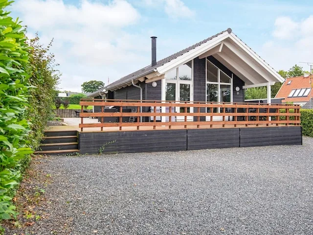 A dark-sided house with a raised wooden deck and gravel driveway.