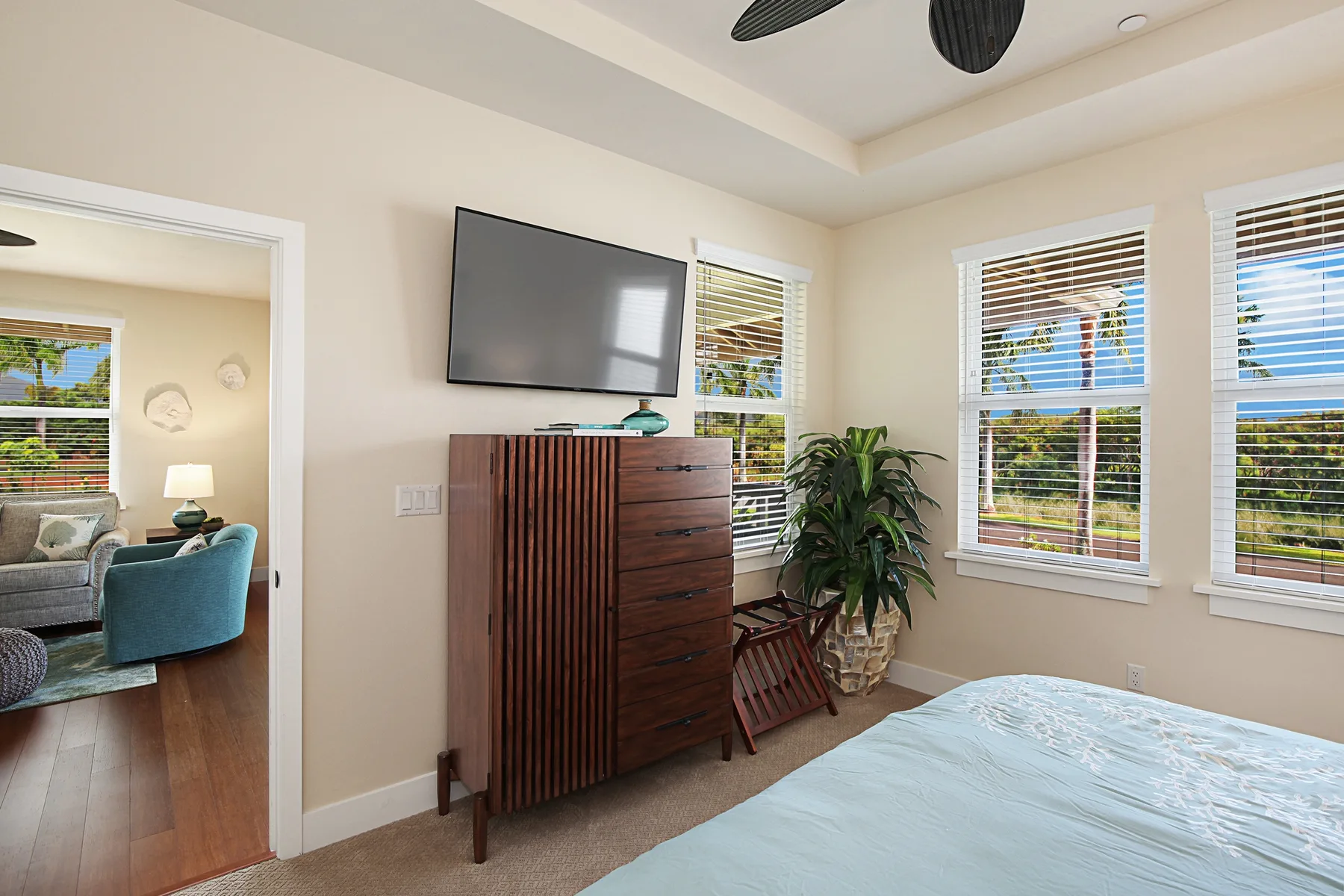 Un dormitorio con una cama, un televisor en la pared, una cómoda de madera y ventanas.