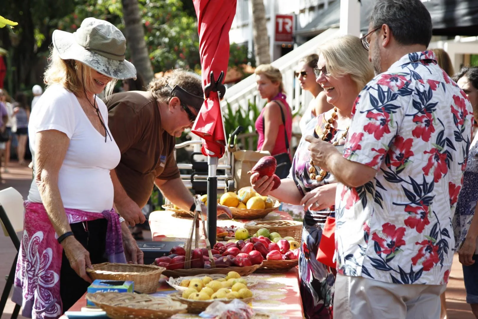 Varias personas miran productos frescos en un puesto de mercado al aire libre.