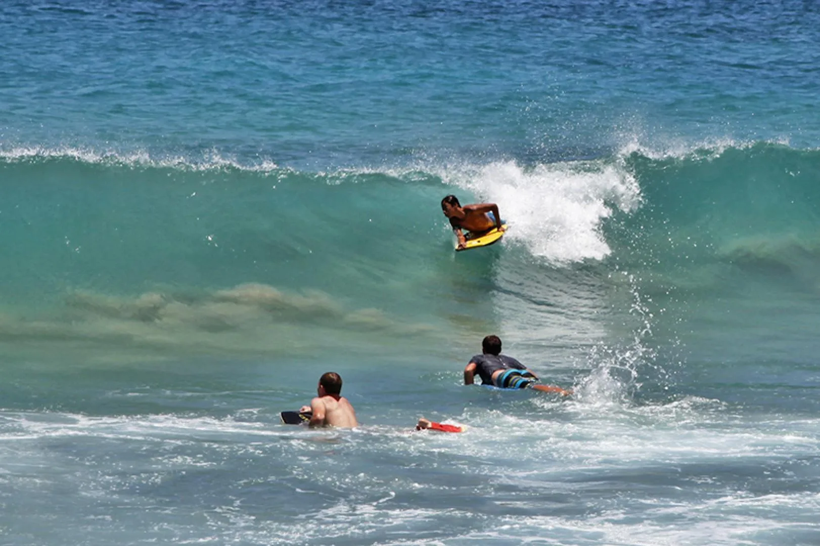 Una persona surfea una ola mientras otras esperan en el mar.