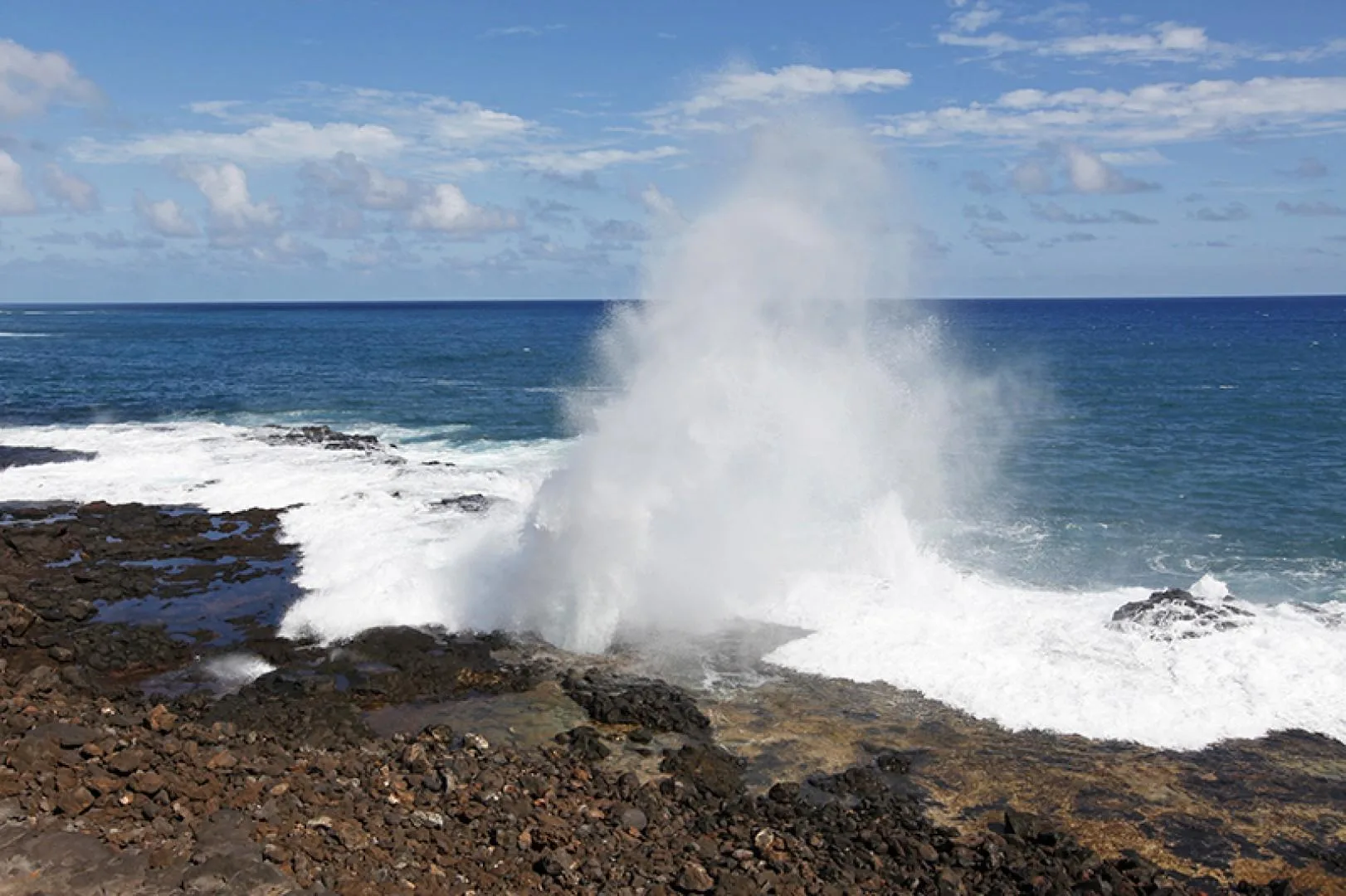 Las olas chocan contra una costa rocosa y lanzan una columna de agua al aire.