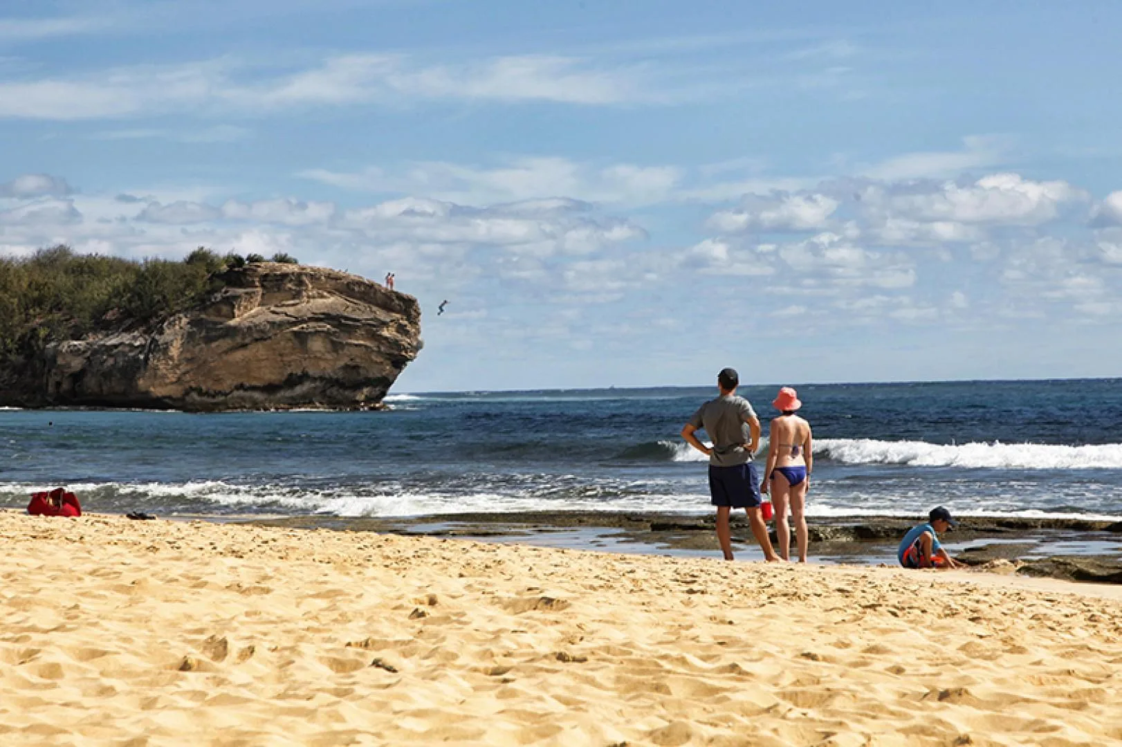 Una playa de arena mira al océano, con personas de pie cerca del agua.