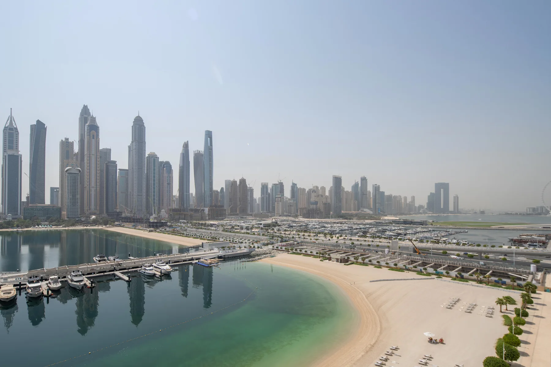 A waterfront city skyline overlooks a curved sandy beach and calm bay.