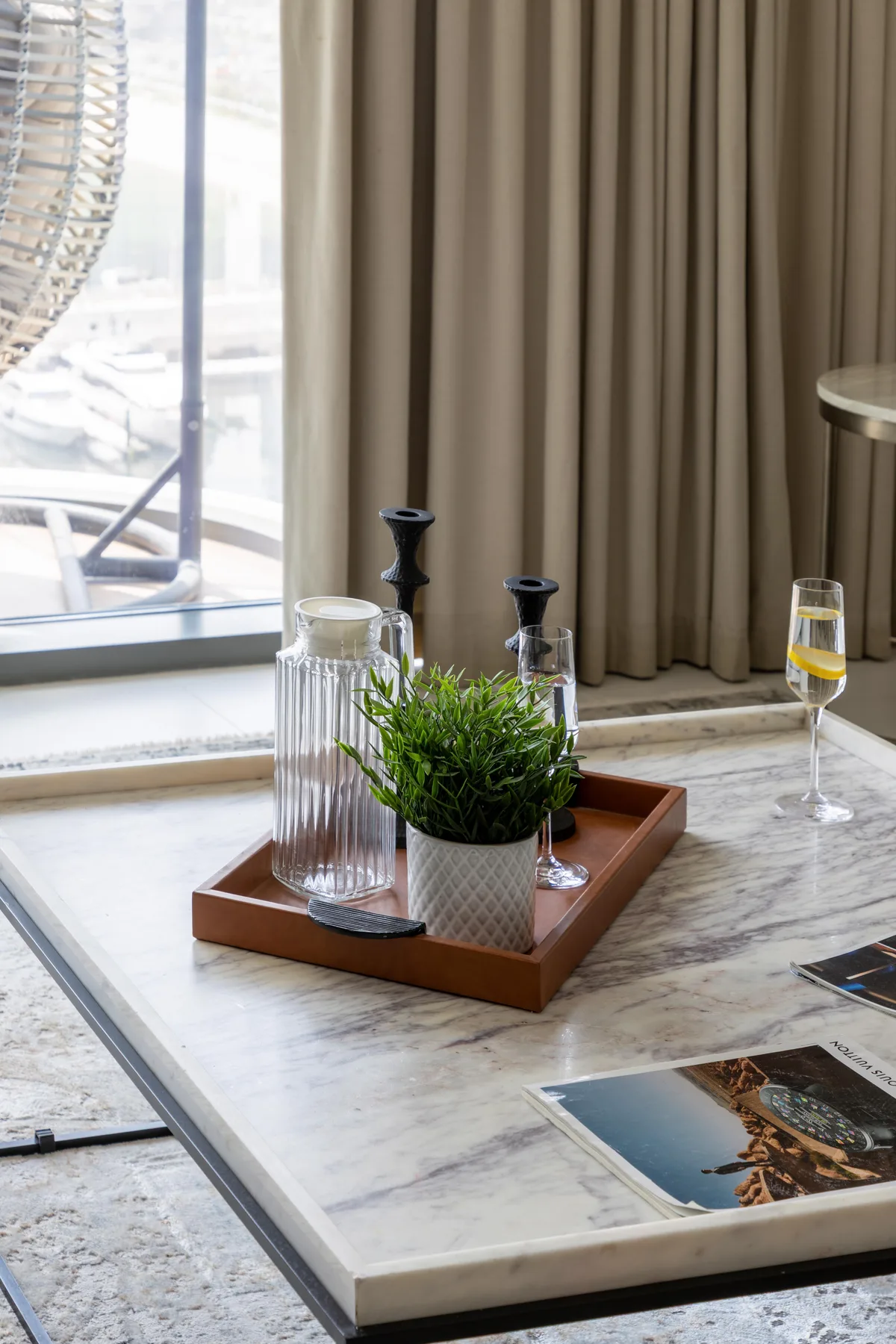 A marble coffee table holds a tray with a plant, glassware, and a drink.