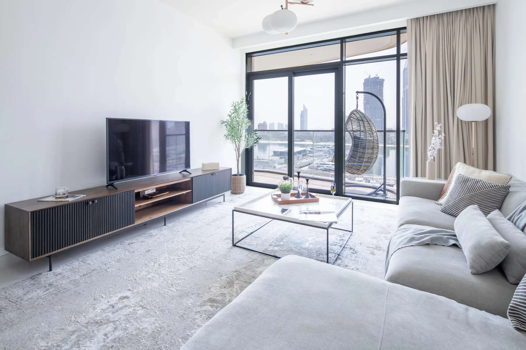 Una sala luminosa con televisor, mesa de centro y ventanas grandes.