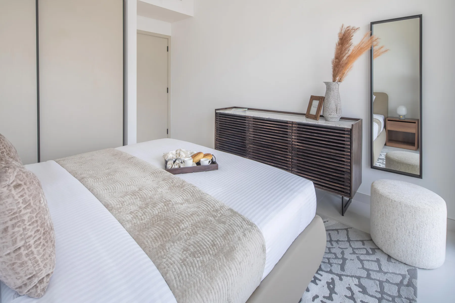 A bright bedroom with a neatly made bed and a dark dresser.