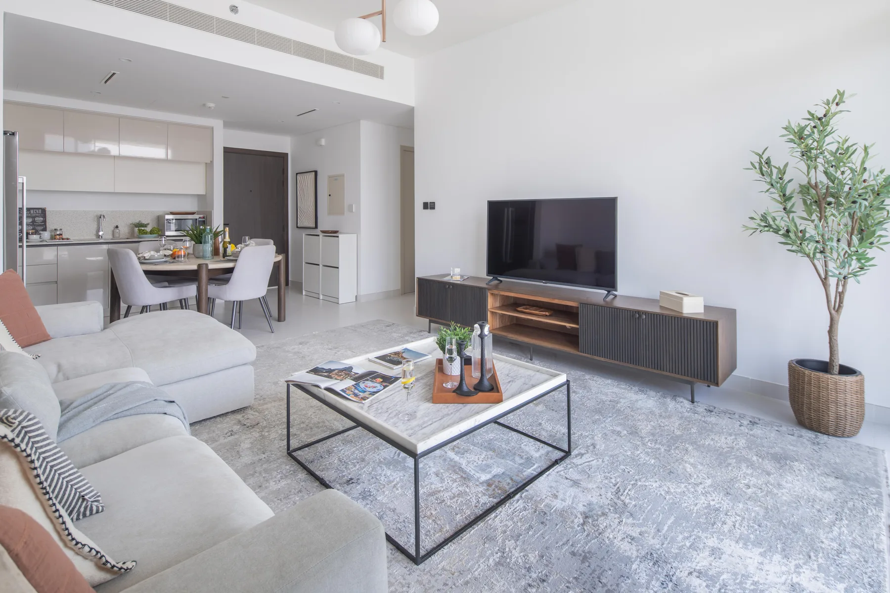 Una sala luminosa con asientos, un televisor y una cocina abierta.