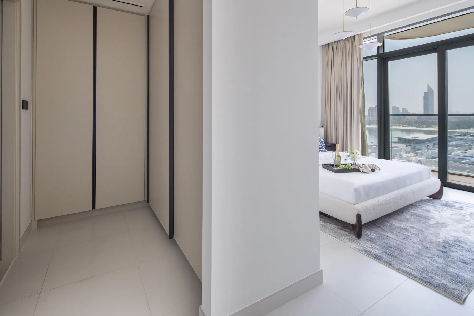 A bedroom with a bed beside a large window overlooking the city.