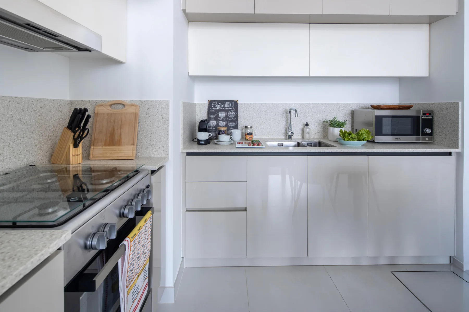 A modern kitchen with white cabinets, a cooktop, and countertop appliances.