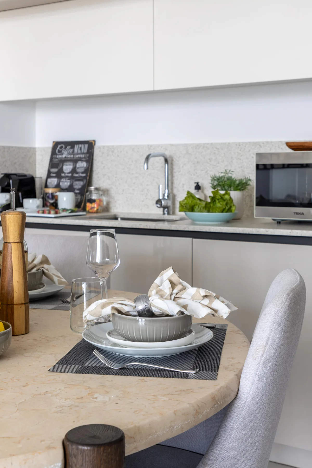 A dining table is set with dishes in front of a modern kitchen.