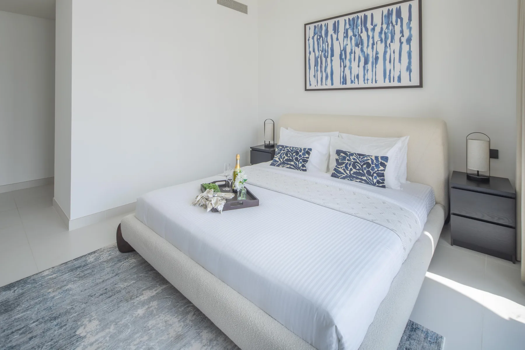 A bright bedroom with a neatly made bed and framed artwork above the headboard.