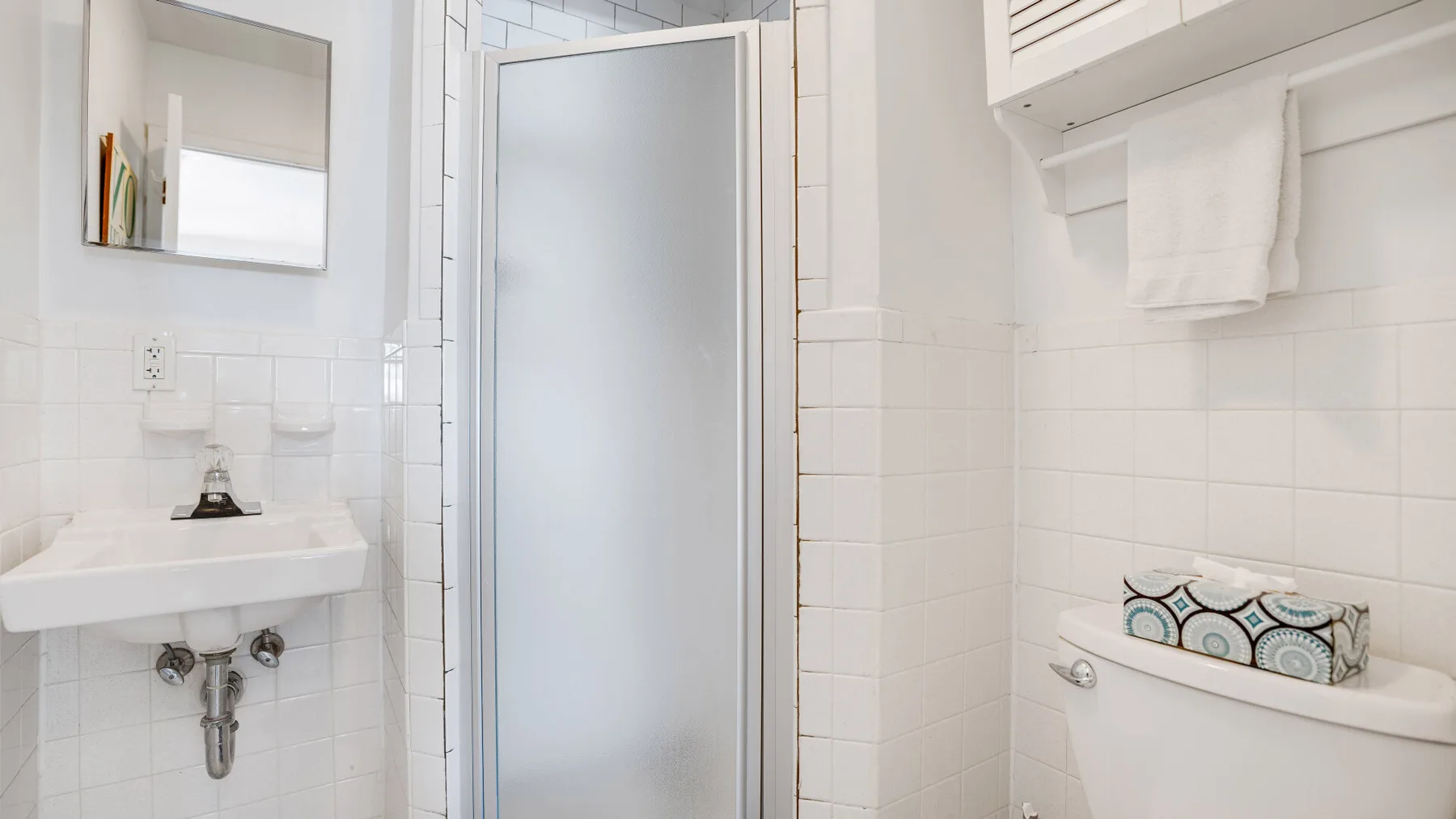 A bright bathroom with a wall-mounted sink and a frosted shower door.