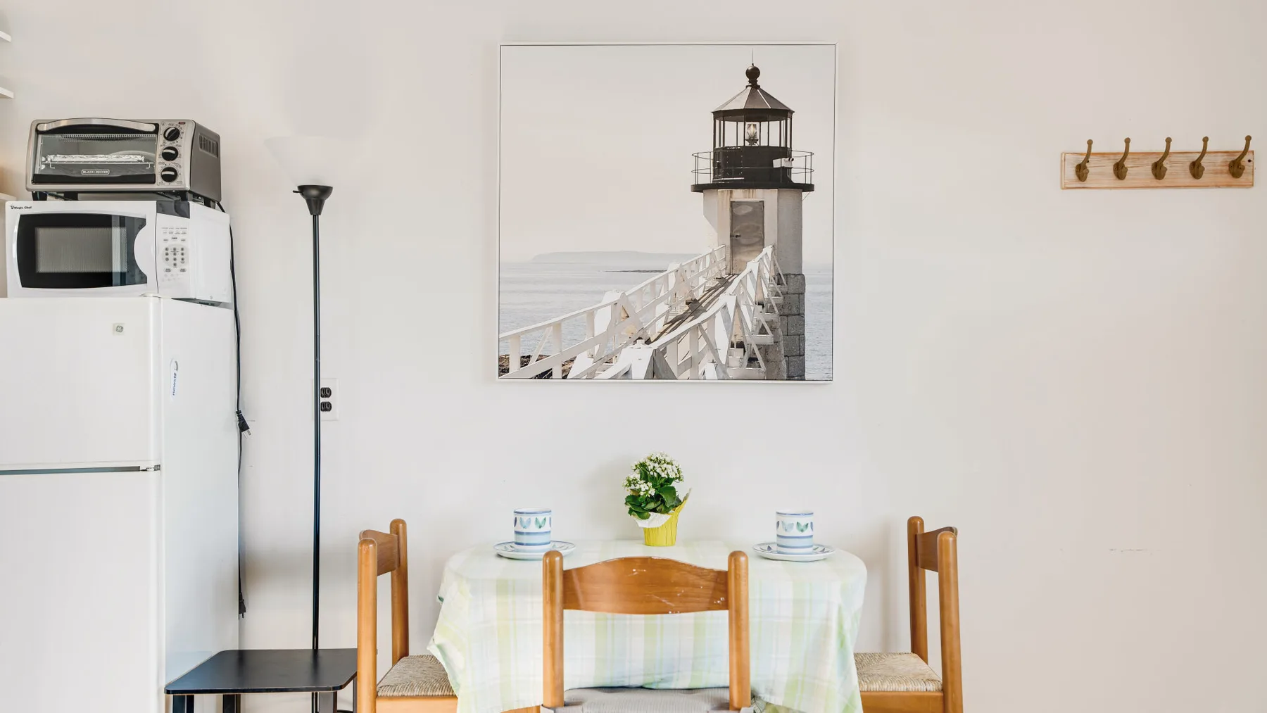 A dining area with a table set beneath a framed lighthouse picture.