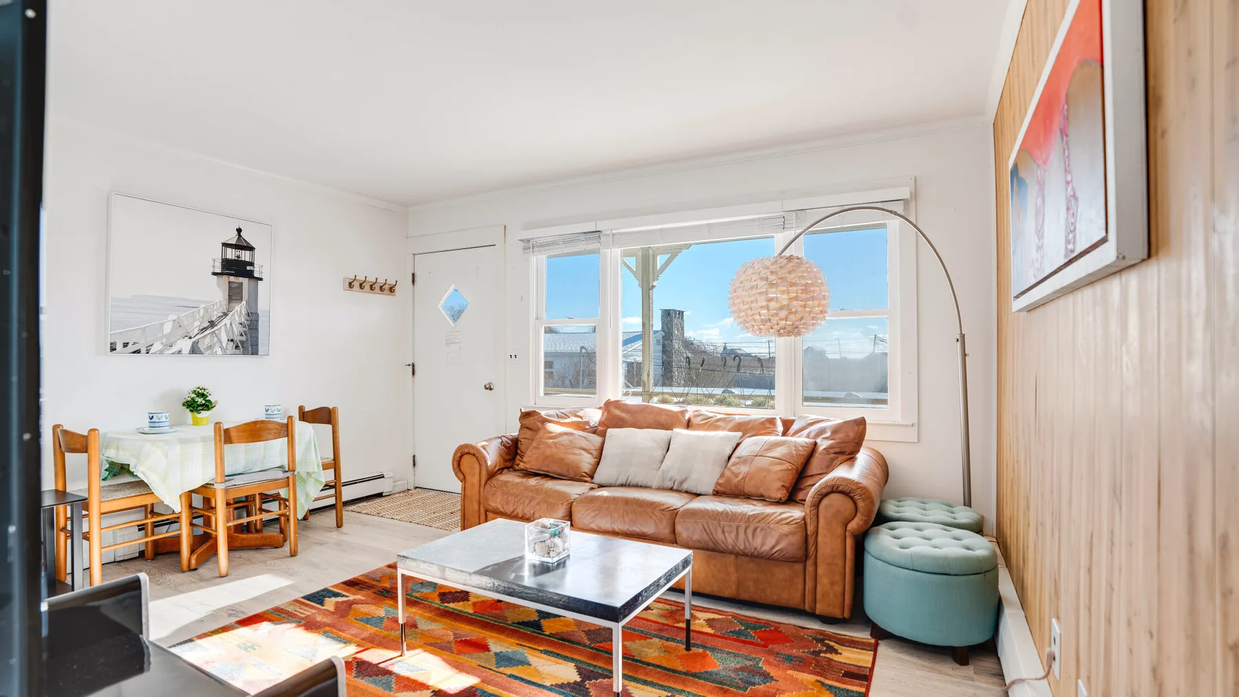 A bright living room with a brown sofa, colorful rug, and large windows.