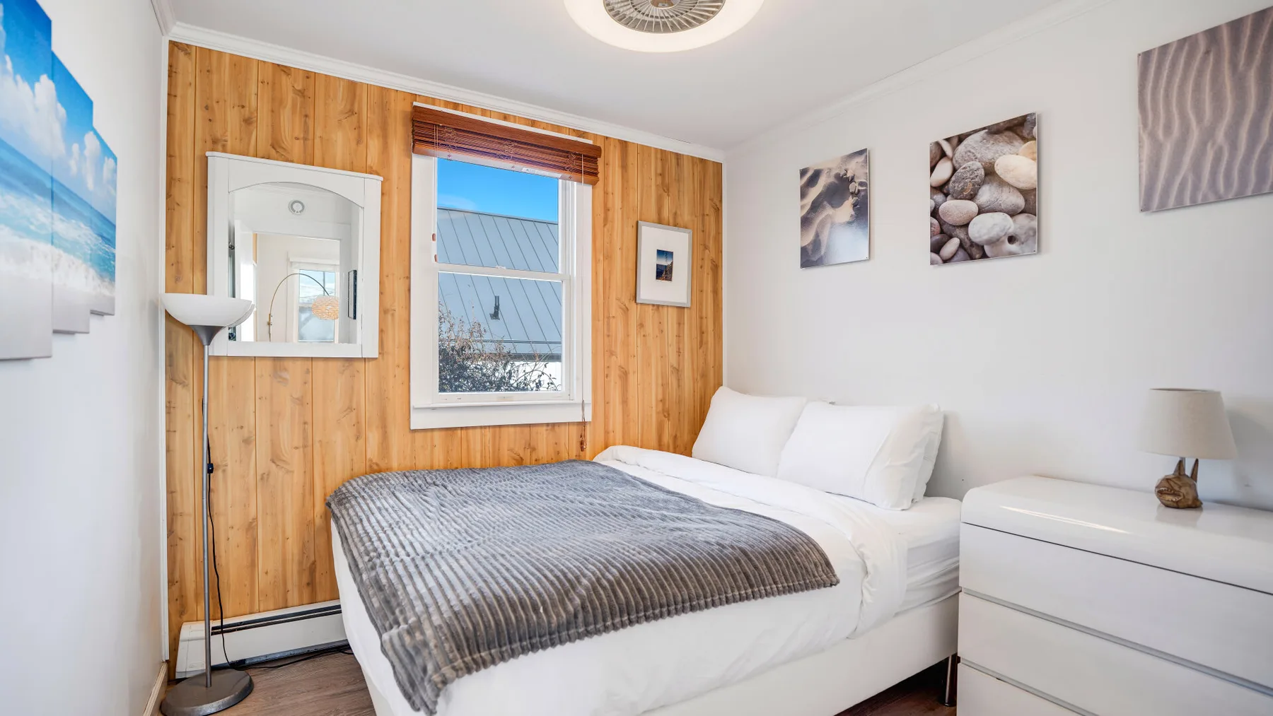 A bright bedroom with a bed, white bedding, and wood-paneled walls.