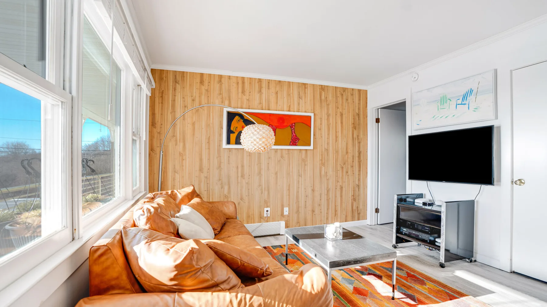 A bright living room with a brown sofa, large windows, and a television.