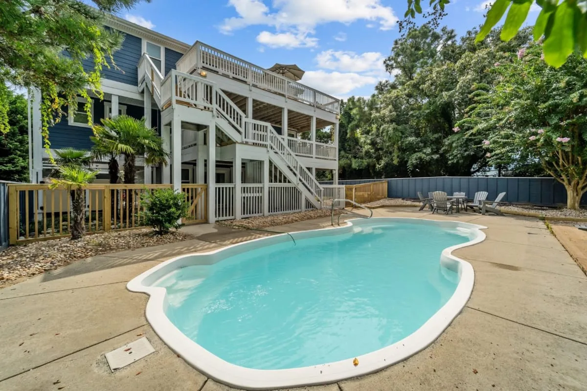 An outdoor swimming pool sits beside a multi-level house with white balconies.