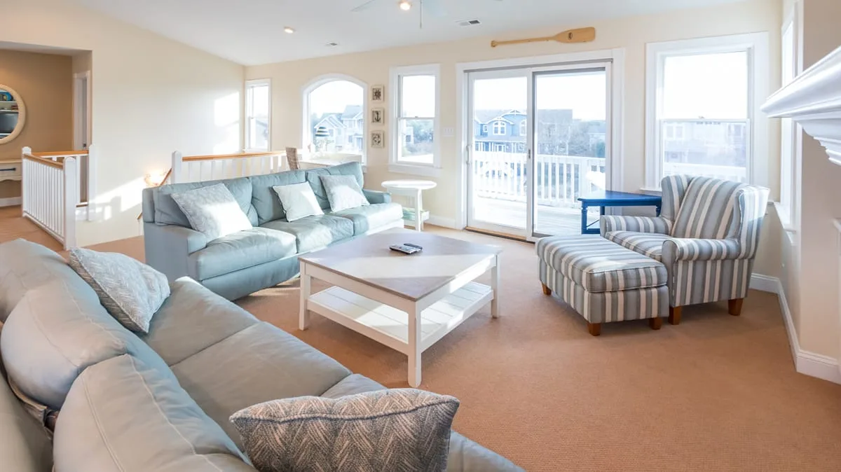 A bright living room has sofas, a striped armchair, and large windows.