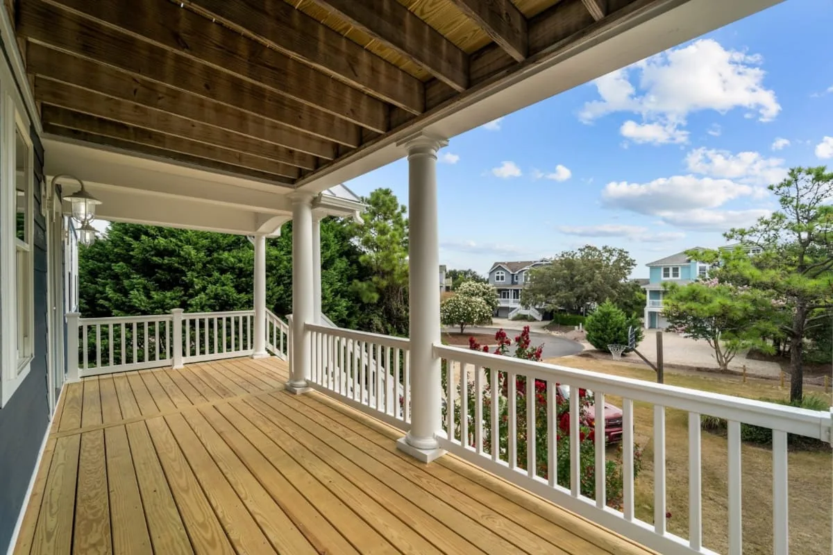 A covered wooden deck overlooks trees, a road, and nearby houses.
