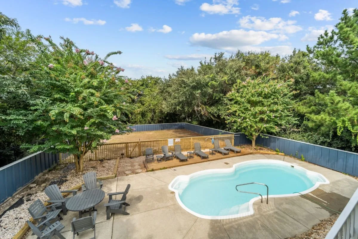 A small outdoor swimming pool sits beside a patio with lounge chairs and greenery.