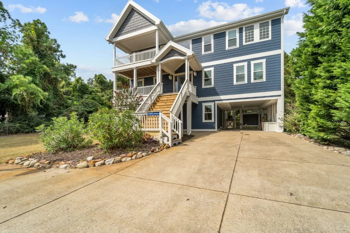 A blue multi-story house faces a wide concrete driveway, with stairs leading to the entrance.