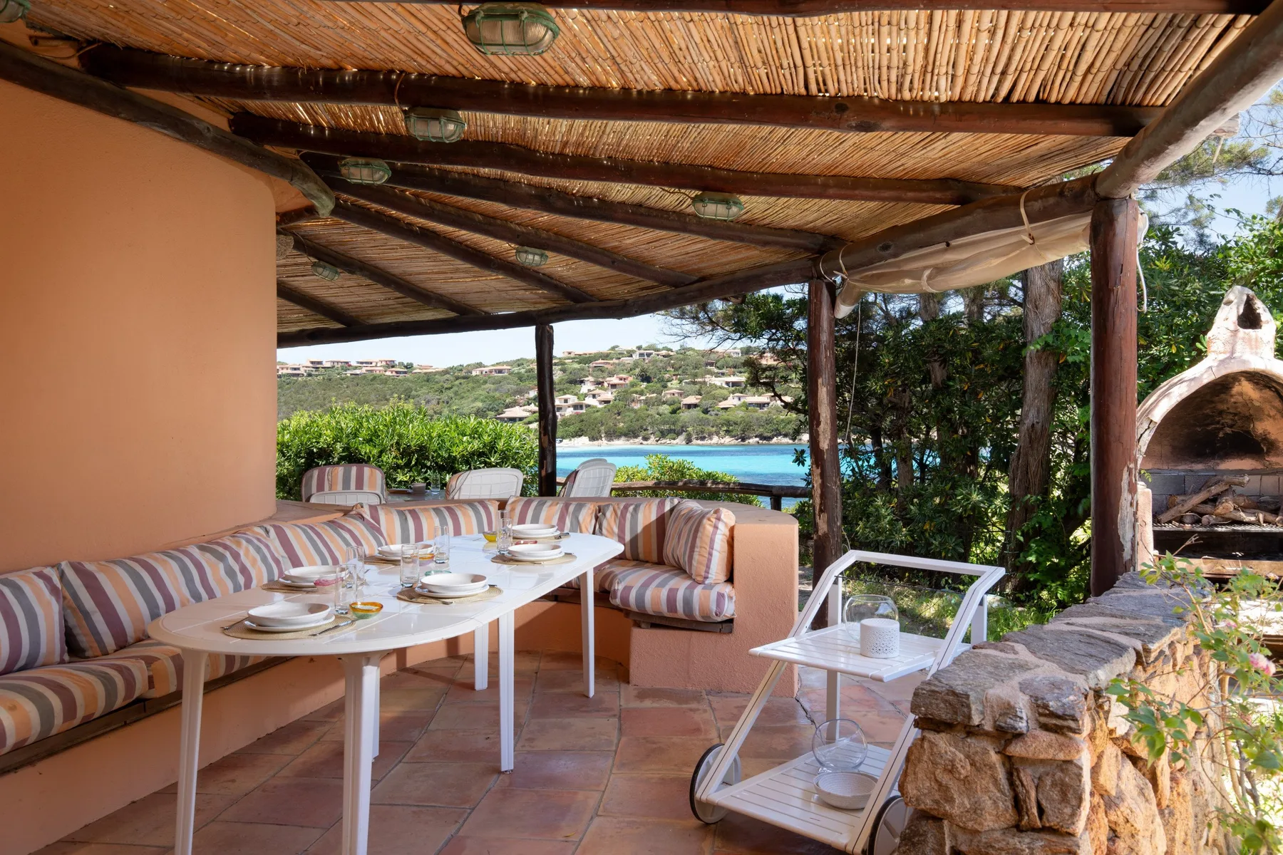 Un comedor exterior cubierto con una mesa y asientos a rayas da a una piscina.