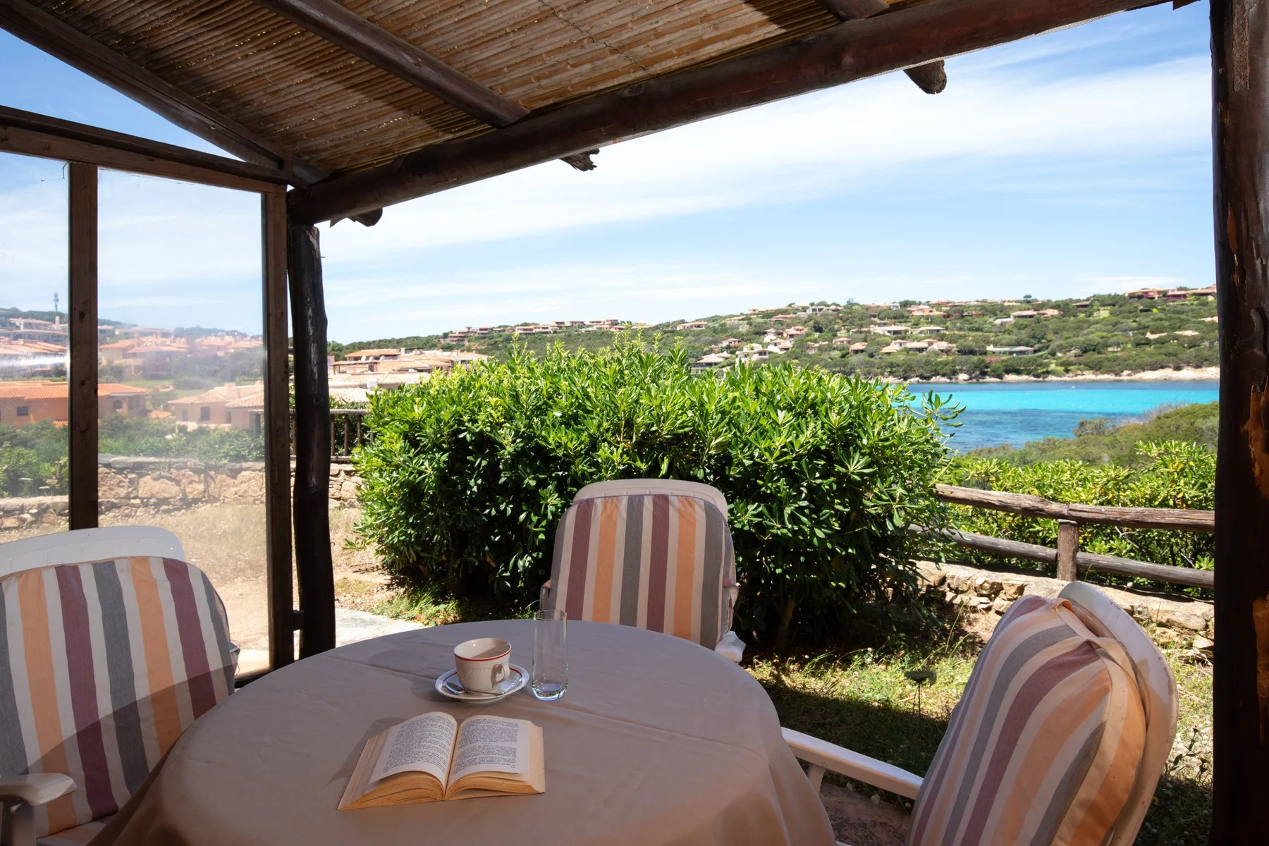 Una zona de comedor cubierta da a colinas verdes y una costa azul.