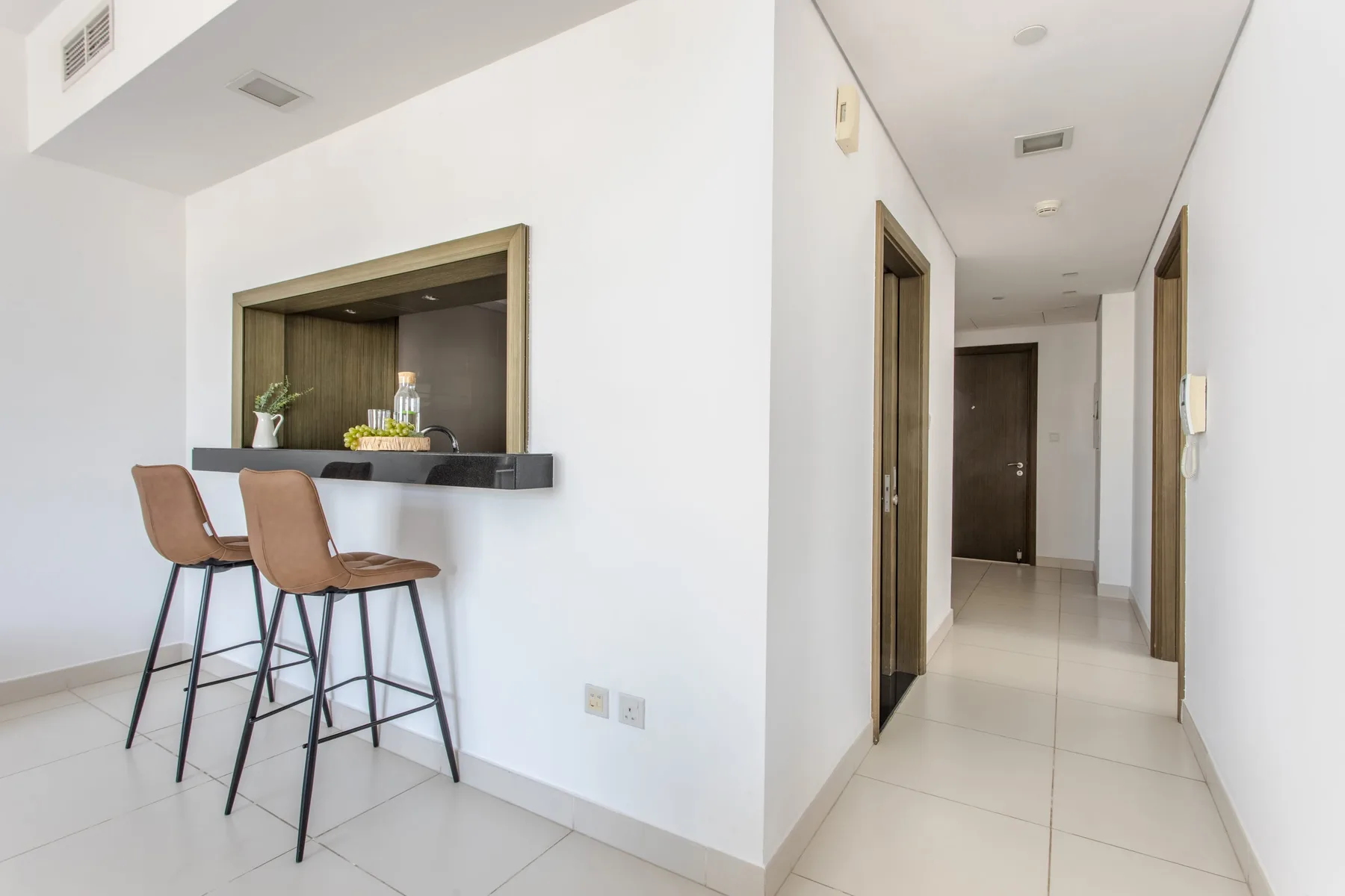 A bright interior shows a small counter with seating beside a hallway.