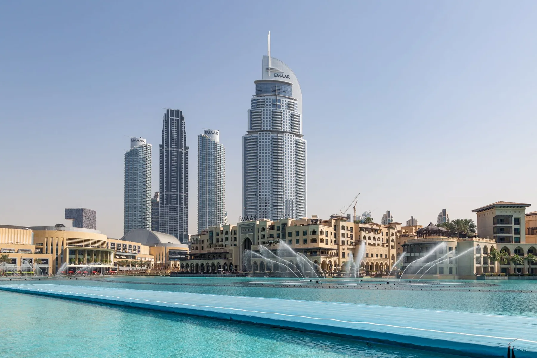 A city skyline rises behind a broad turquoise pool with fountains.
