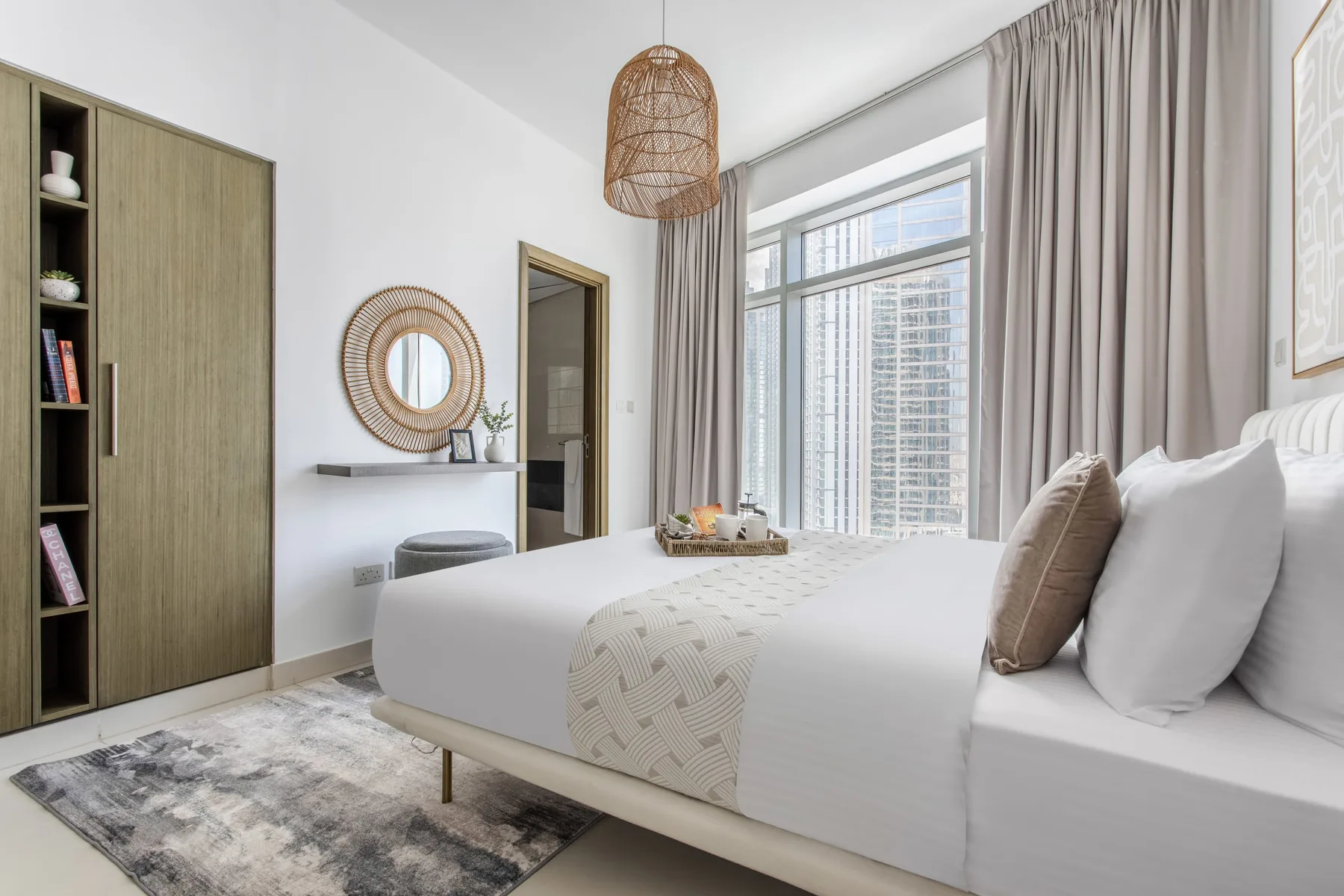 A bright bedroom with a neatly made bed beside large curtained windows.