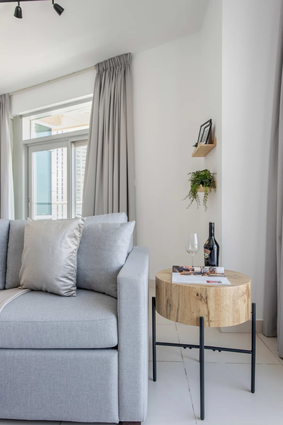 Una sala luminosa con un sofá gris junto a una mesa auxiliar redonda de madera.