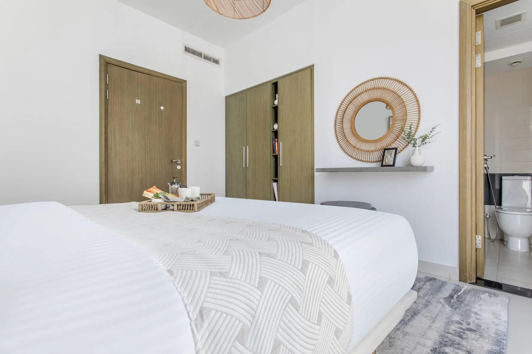 A bright bedroom with a neatly made bed and a doorway opening onto a bathroom.