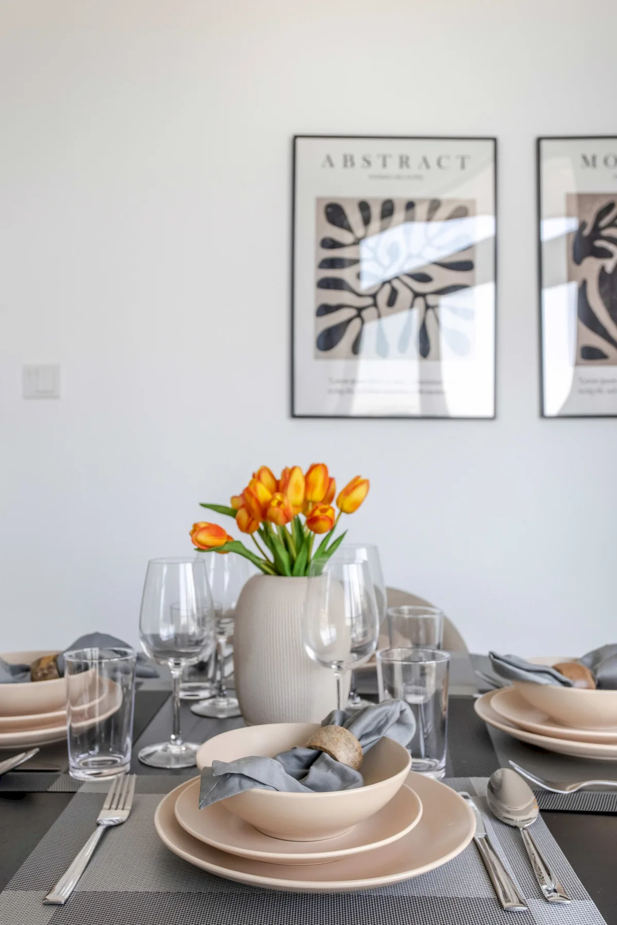 A dining table is set with plates, glassware, and a vase of orange flowers.
