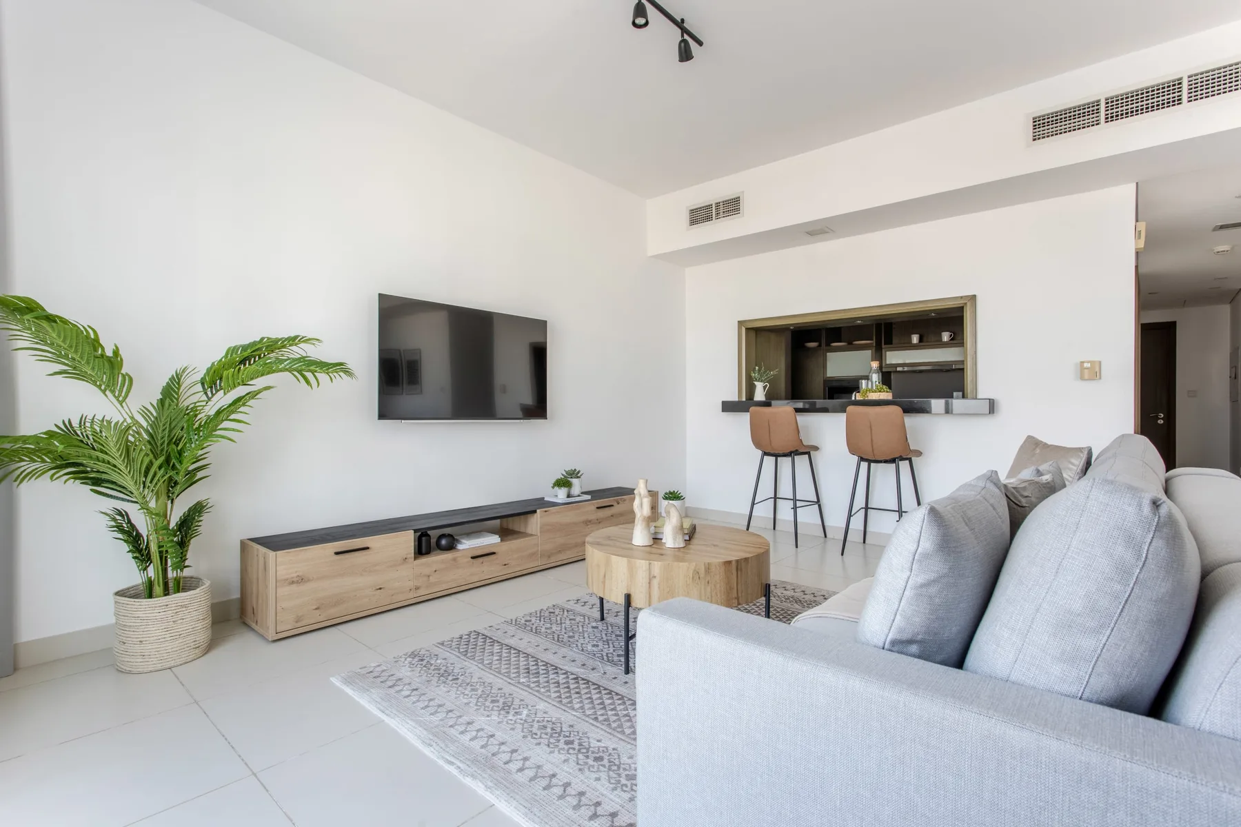 A bright living room with a seating area, television, and kitchen bar.