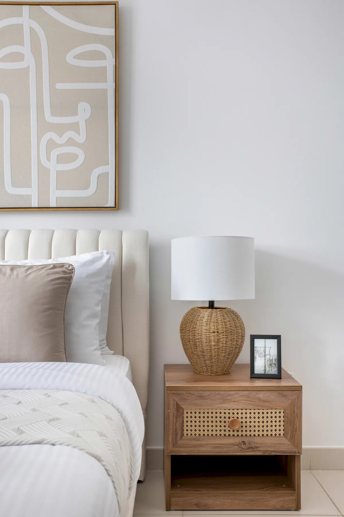 A bright bedroom with a bed beside a wooden nightstand and table lamp.