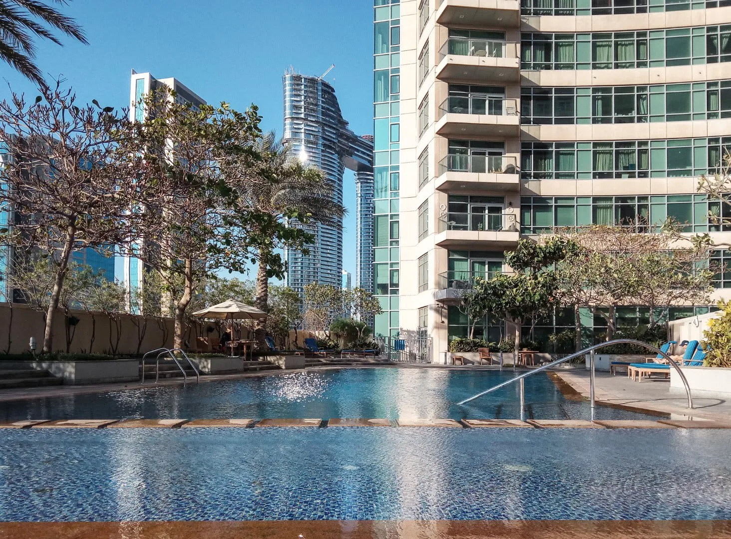 An outdoor swimming pool sits beside a modern high-rise building.