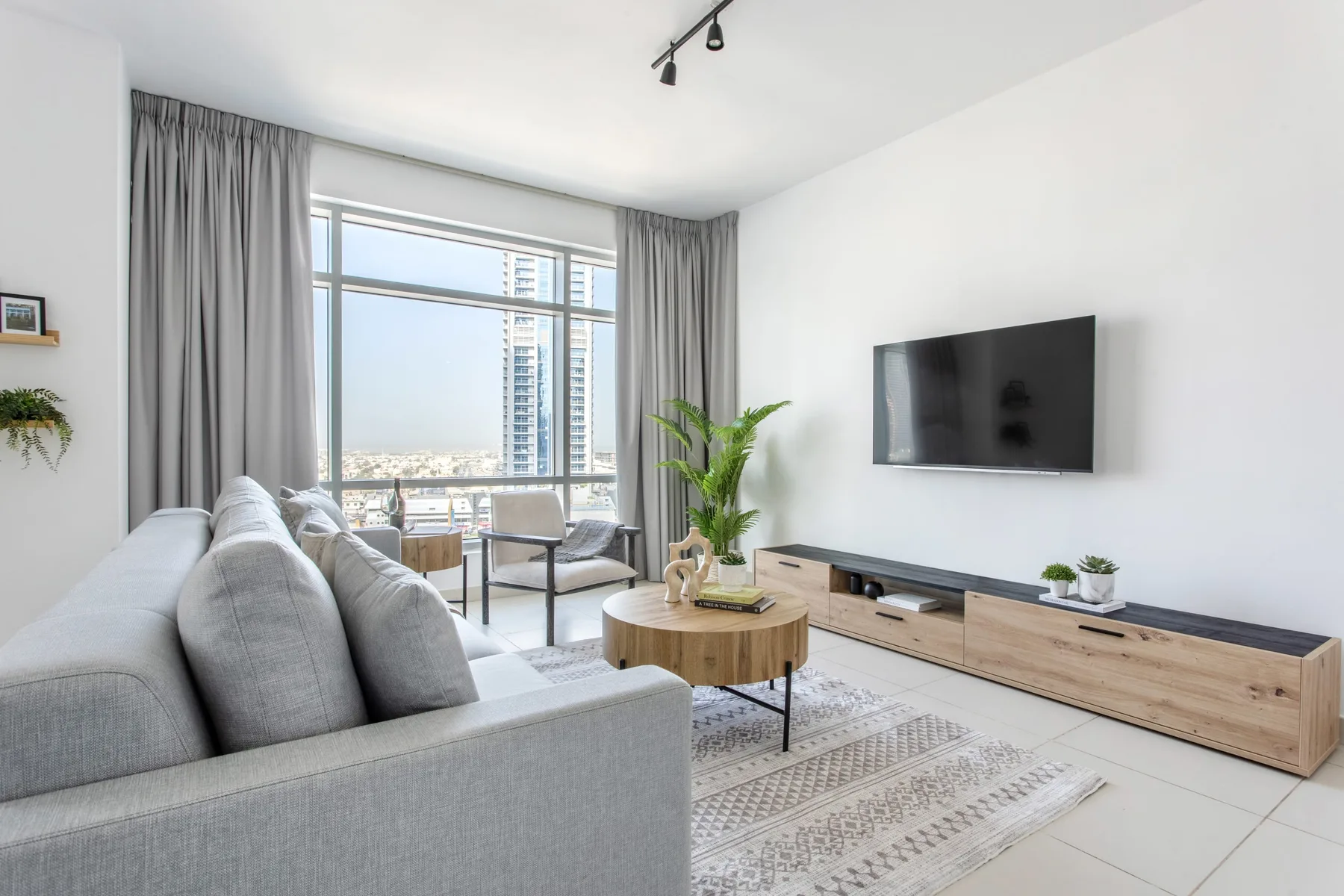 Una sala luminosa con asientos grises, un televisor y ventanales.