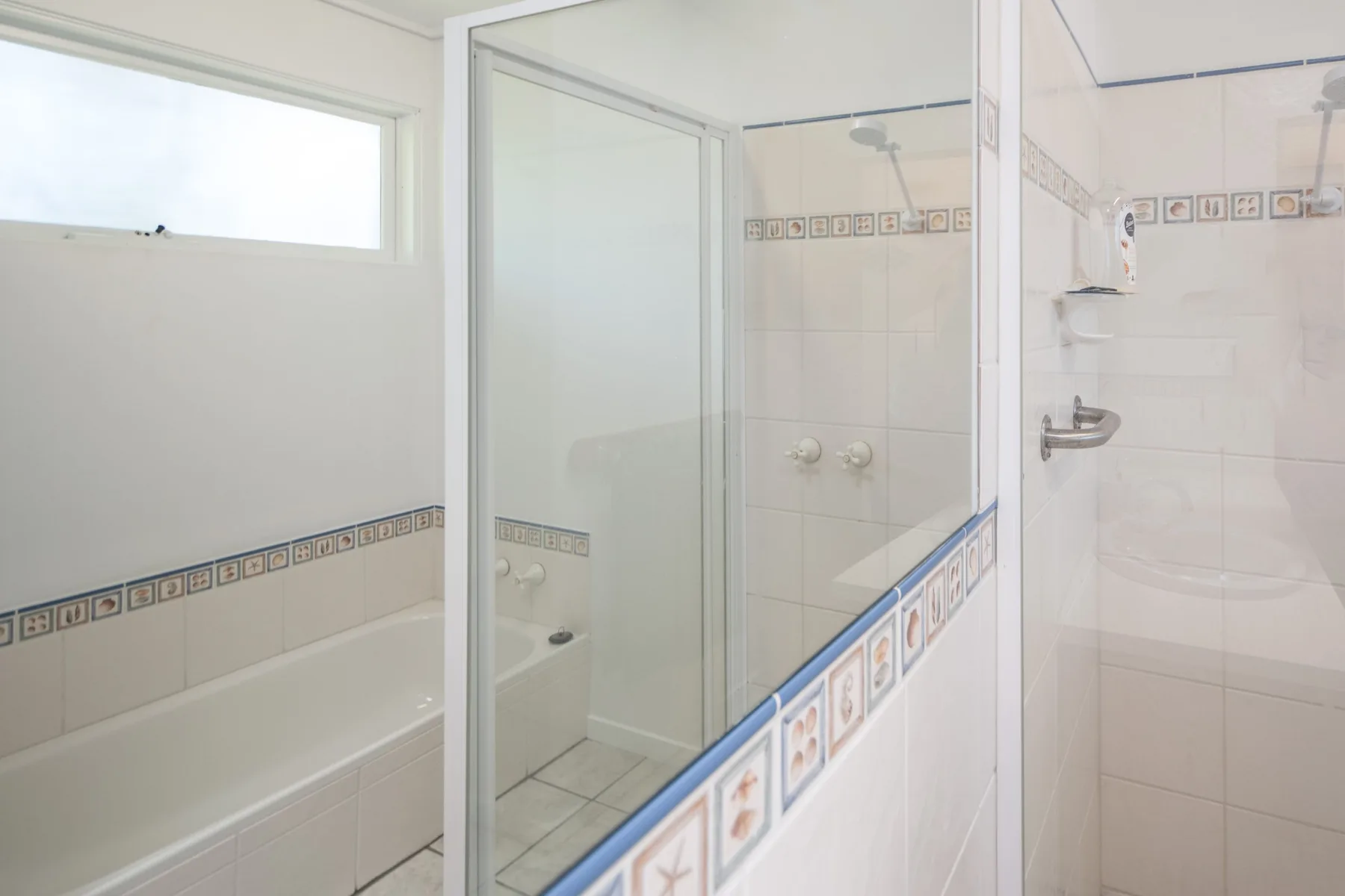 Un baño alicatado con bañera y mampara de ducha de vidrio.