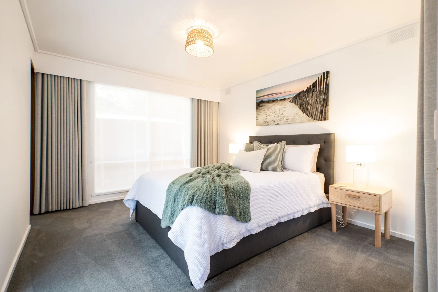 Un dormitorio luminoso con una cama bien tendida y una gran ventana con cortinas.