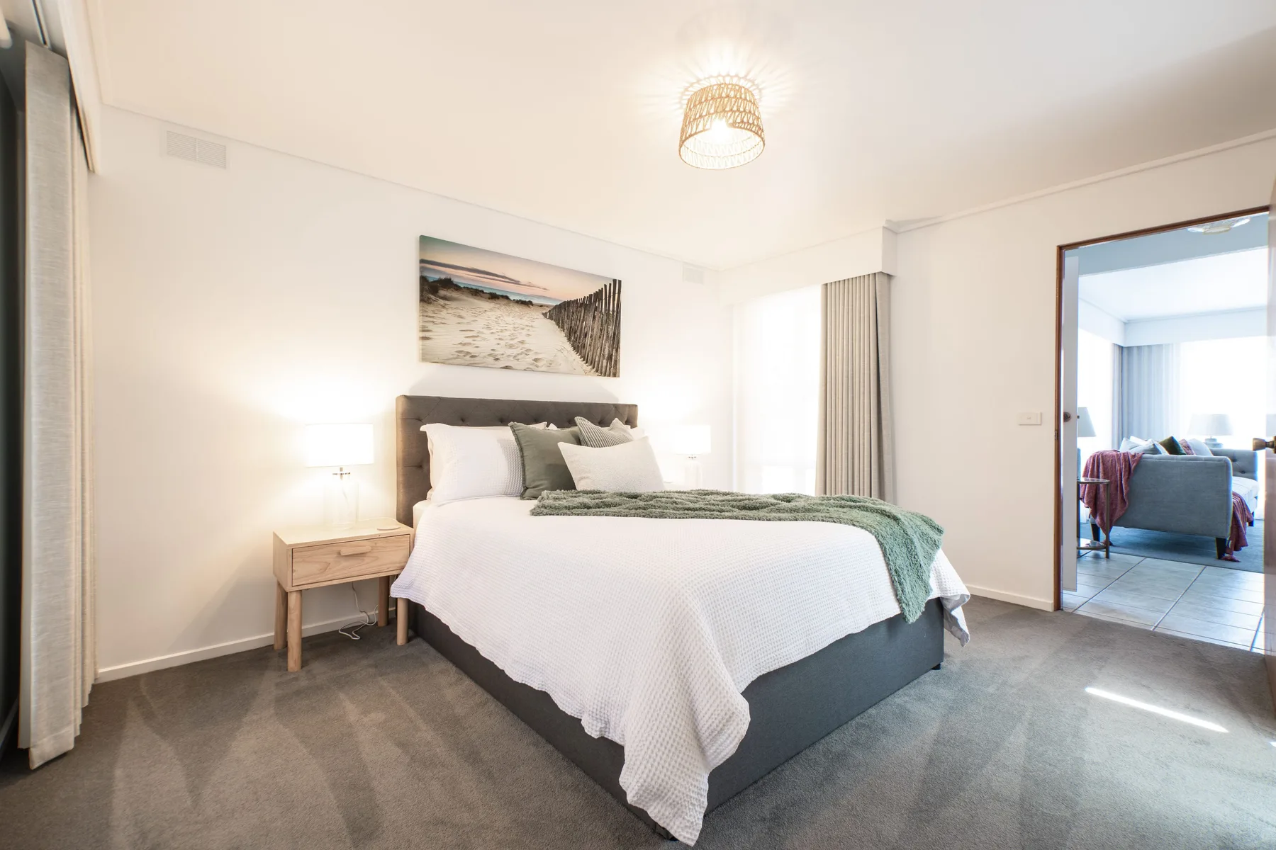 Un dormitorio luminoso con una cama bien arreglada y una puerta a otra habitación.