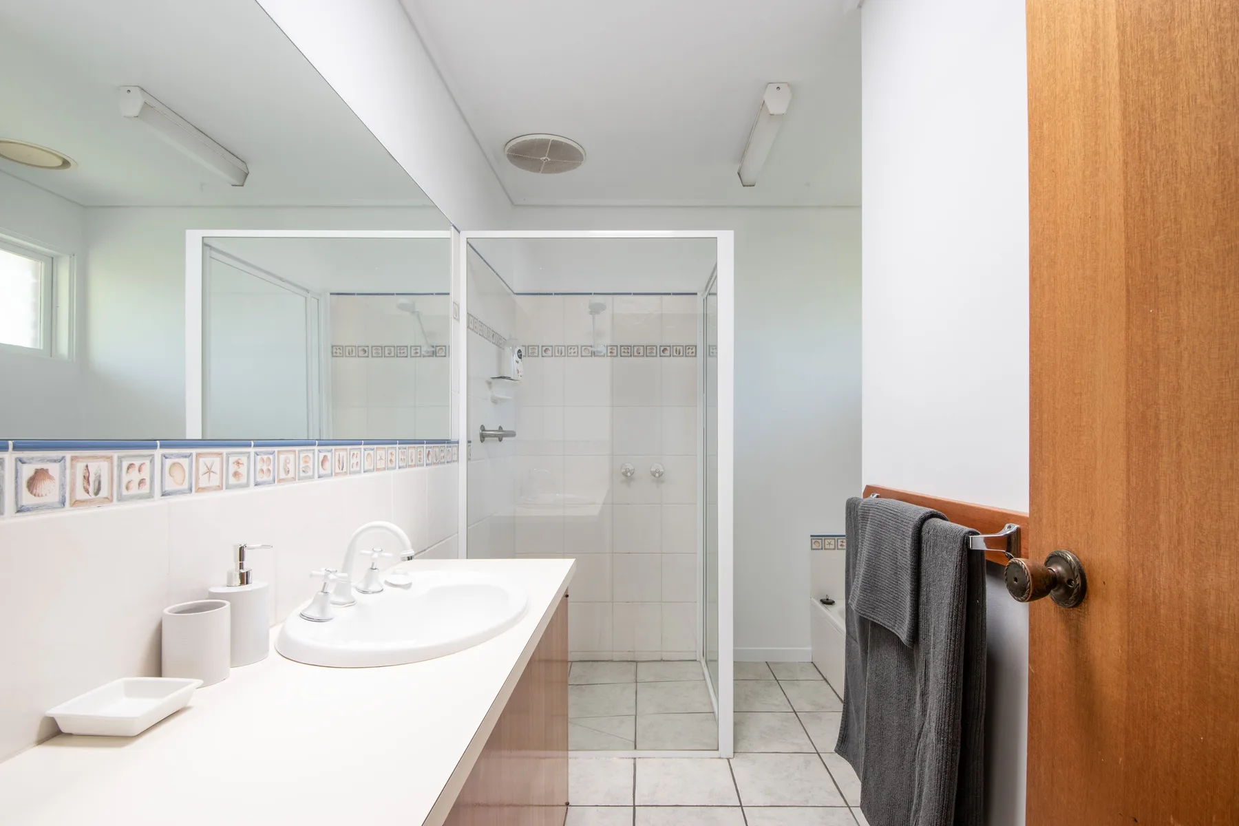 Un baño luminoso con un lavabo largo y una ducha de vidrio.